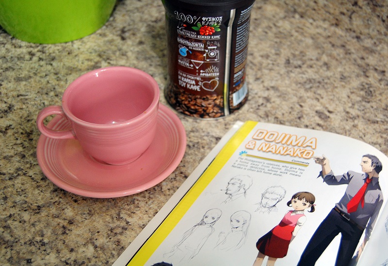 Persona 4 artbook open next to a coffee cup and instant coffee, with Dojima and Nanako pictured