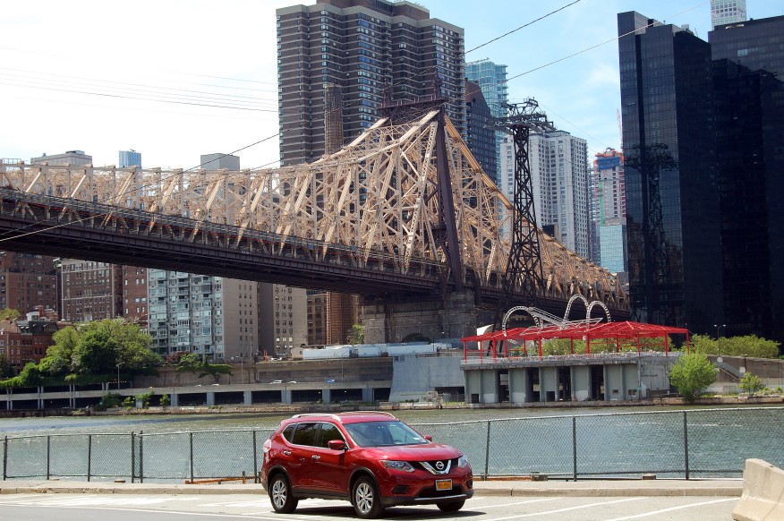Photo of a red car on Roosevelt Island with the Queensboro Bridge and Manhattan in the background.  Taken by N.A. Ferrell on June 8, 2019.