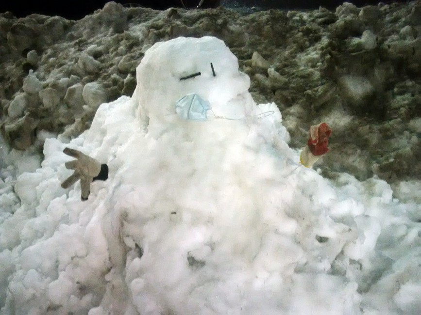 A horrifying snowman with a surgical mask in front of a black snowbank, photographed by Nicholas A. Ferrell in Cobble Hill, Brooklyn, on February 4, 2021.