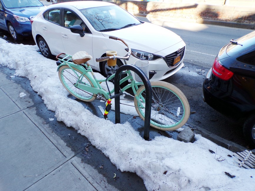 A mint bike sitting in the midst of snow in Brooklyn's Columbia Street Waterfront District.