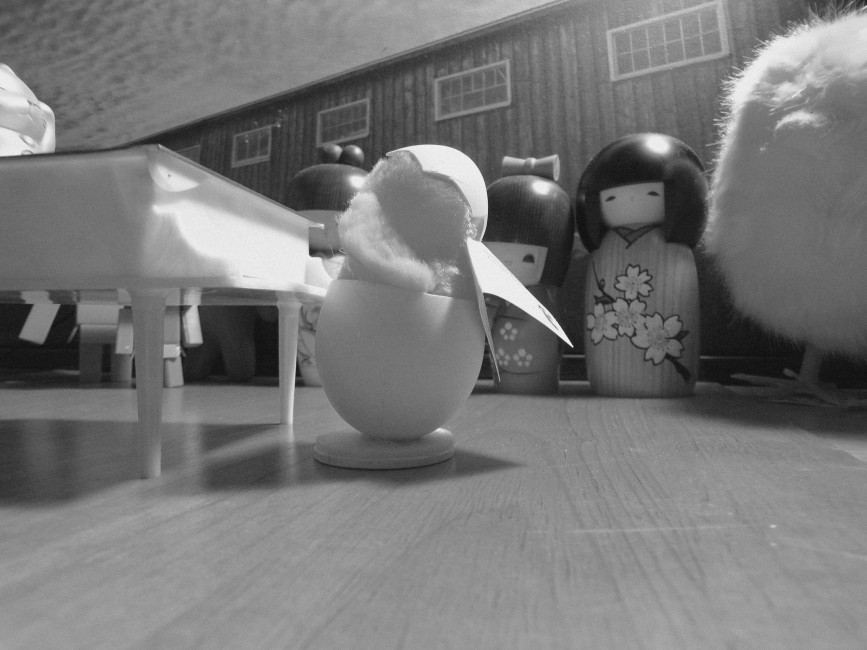 A toy hatchling plays a piano as a larger stuffed chick watches.