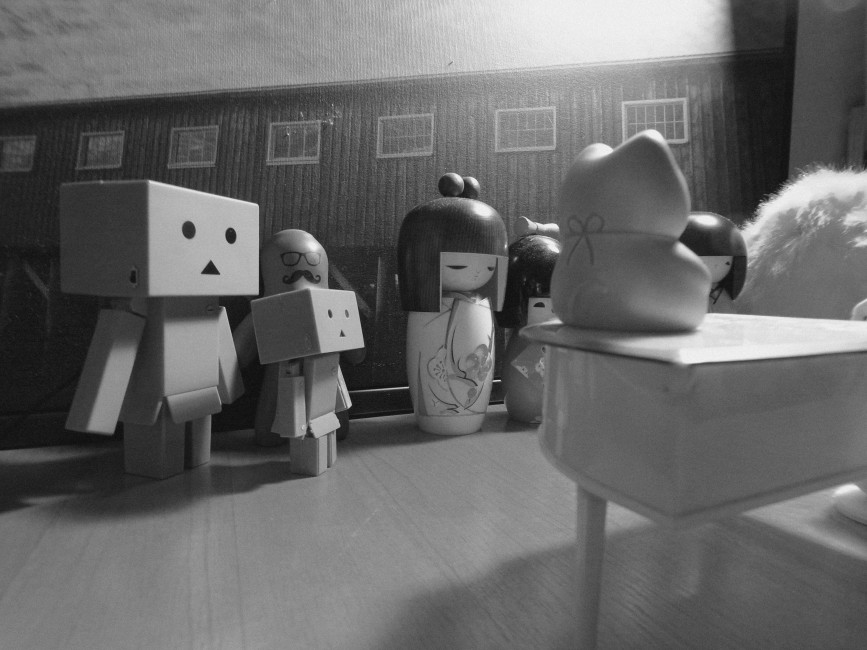 Two danbo and a few kokeshi dolls watch a hatchling play piano.
