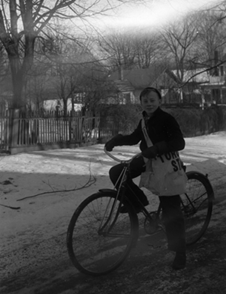 Photograph of a young paperboy in Ontario, Canada, on his bike with a bag full of newspapers, in 1940