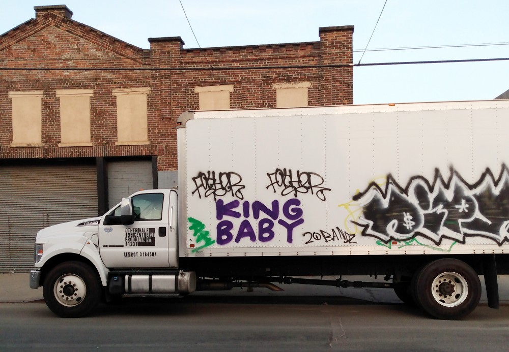 A commercial truck covered in graffiti parked in Gowanus, Brooklyn.  The purple "KING BABY" graffiti looks new and stands out.