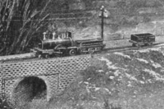1895 photo of a miniature model train crossing a mini model bridge.