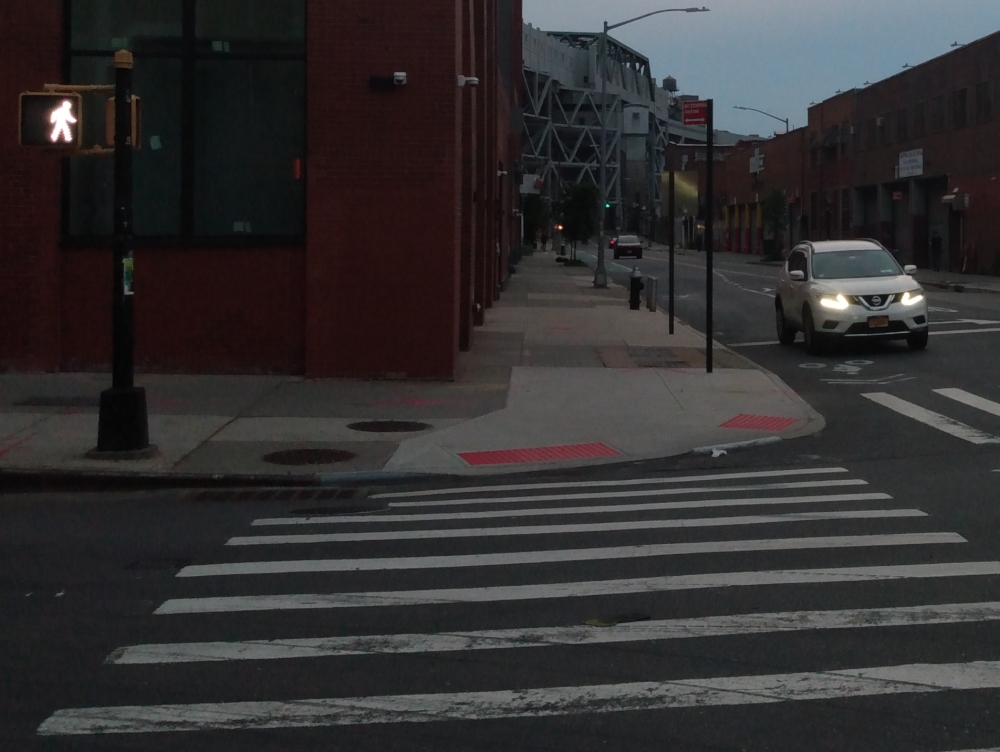 A photo of a street crossing on West 9th Street in Gowanus, Brooklyn, with a car with bright headlights on the right side of the photo.