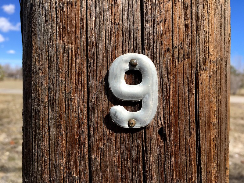 A metal number nine nailed to a post in the desert.  "Number 9" by cogdogblog is marked with CC0 1.0