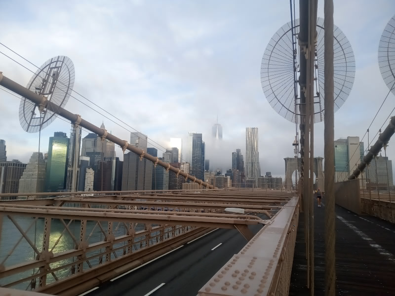 Photo of the Manhattan Skyline, shrouded in fog, from between the first and second towers of the Brooklyn Bridge.
