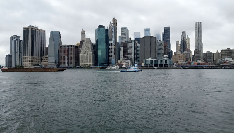 Nicholas A. Ferrell's photograph of a powder blue and white tugboat pulling a barge up the East River with the Manhattan skyline in the background.