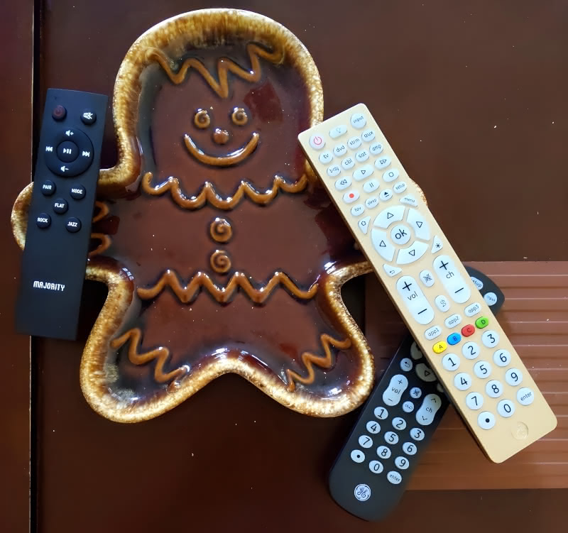 A gingerbread man plate "holding" a Majority Bowfell soundbar remote and two GE universal remotes.