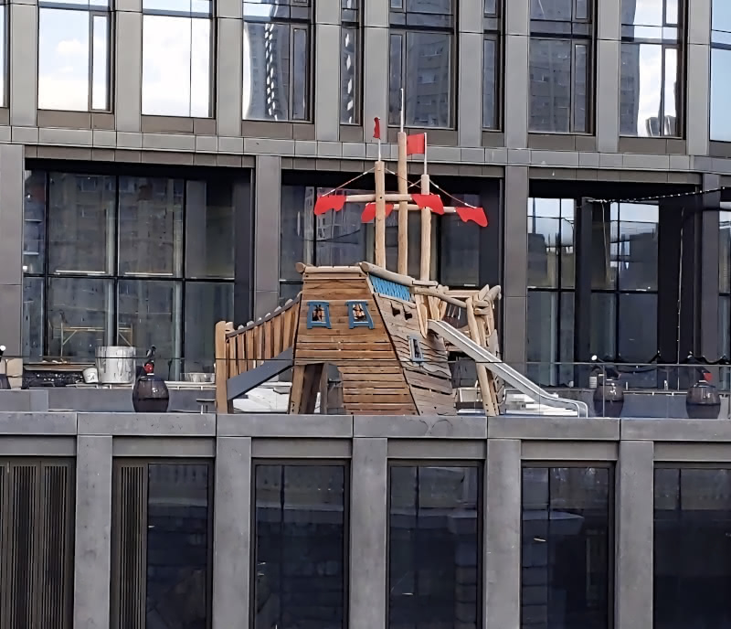 Photo of a playground in the shape of a boat on the balcony of a DUMBO Brooklyn apartment building, seen from the Brooklyn Bridge.  This view shows the back of the boat.