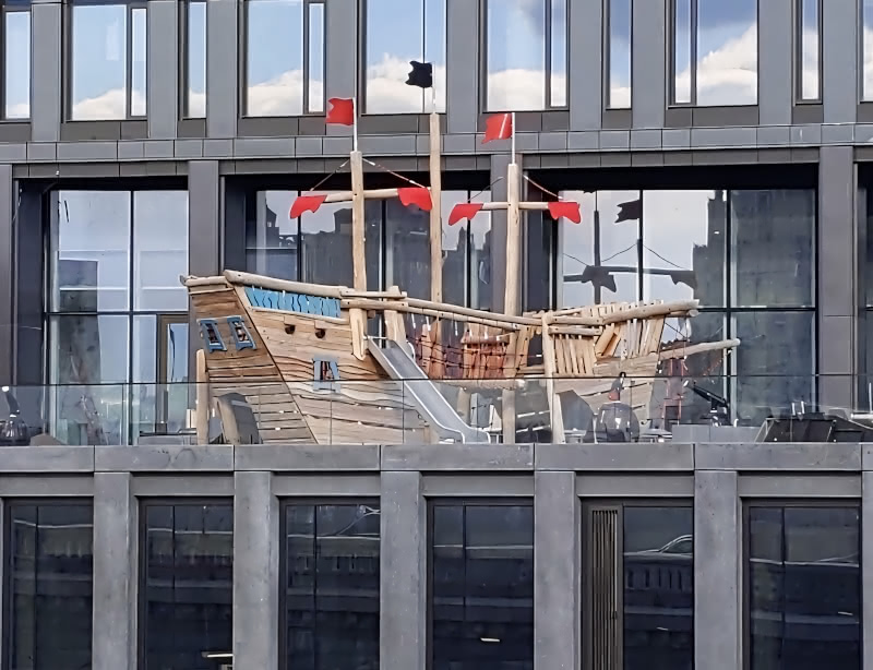 Photo of a playground in the shape of a boat on the balcony of a DUMBO Brooklyn apartment building, seen from the Brooklyn Bridge. From this angle, it is hard to see that the boat is a playground.