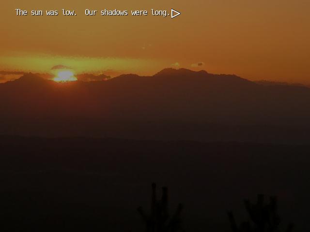 Scene from The Letter visual novel. The background is a setting sun falling behind mountains. The sky is orange.  The text reads "The sun was low. Our shadows were long."