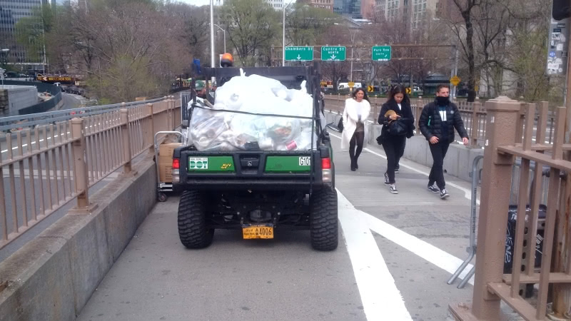 2019 photograph of a small NYC DOT pick up full with bags of trash on the pedestrian walkway of the Brooklyn Bridge between the two Manhattan exits.