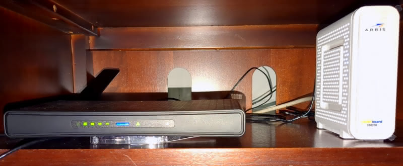A Mikrotik hAP ac3 router sitting next to an ARRIS SURFboard SB8200 modem on a wooden shelf.