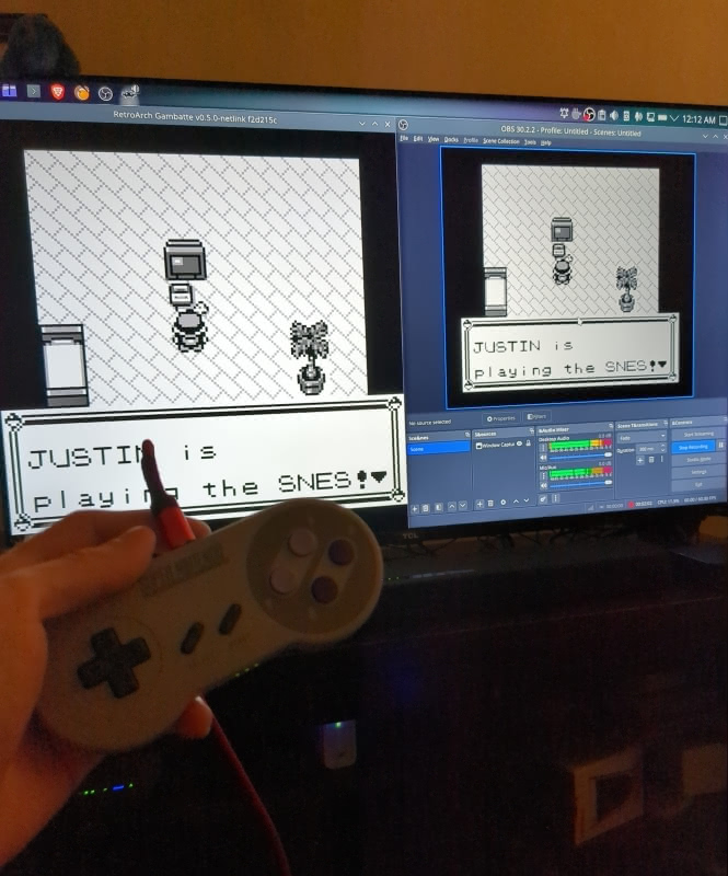 Photograph of my hand holding a Nintendo Switch Online SNES controller with a TV in the background. The TV is showing Pokemon Red being played on the Ganbatte emulator. The left side of the screen shows the first scene in the game with the player character in his bedroom interacting with an SNES. The right side of the screen shows the same thing in OBS.