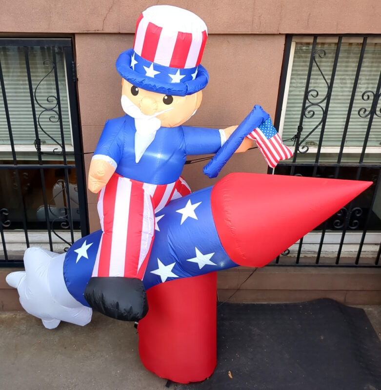 An inflatable decoration depicting Uncle Sam riding a red white and blue rocket while waving an American flag.