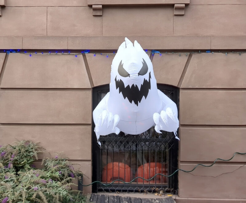 A large white inflatable ghost stuck to a window so that it looks like it is breaking through the window.