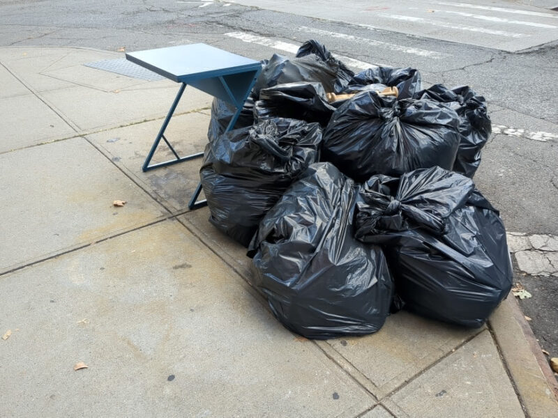 Blue desk with z-shaped legs next to a pile of garbage bags on curb in Columbia Street Waterfront District.