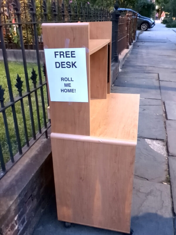 A children's writing desk on the sidewalk outside a home in Carroll Gardens. There is a piece of paper taped to the side of the desk which reads "FREE DESK ROLL ME HOME!" Sure enough, the bottom of the desk does have wheels.