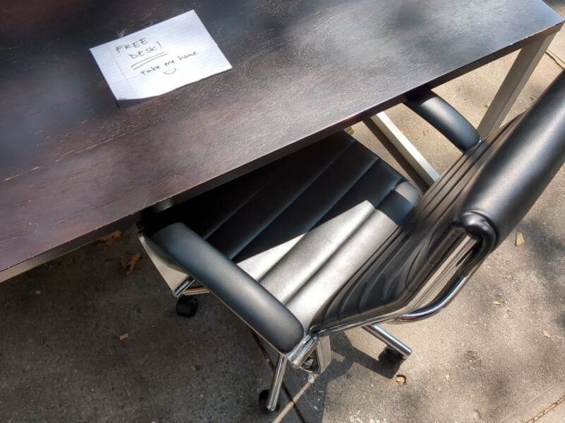 Free brown desk with silver legs and desk chair left on sidewalk in Carroll Gardens. There is a note on top of the desk. It reads "FREE DESK!" and after two underlines "Take me home" with a smiley face.