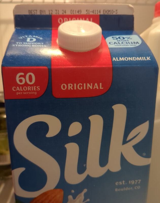 A carton of Silk almond milk in a refrigerator. The sell-by date is 12/31/24.