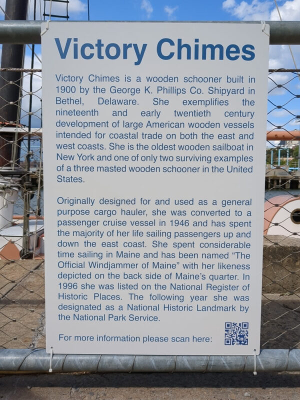 Description of the Victory Chimes schooner posted at Pier 6 of Brooklyn Bridge Park. It notes that "Victory Chimes is a wooden schooner built in 1900 by the George K. Phillips Co. Shipyard" and that "[s]he is the oldest wooden sailboat in New York and one of only two surviving examples of a three masted wooden schooner in the United States." It adds that Victory Chimes was "[o]riginally designed for and used as a general purpose cargo hauler" before, beginning in 1946, being used for "sailing passengers up and down the East Coast." It adds that Victory Chimes is closely associated with Maine, depicted on the back of Maine's state quarter, and listed on the National Register of Historic Places.