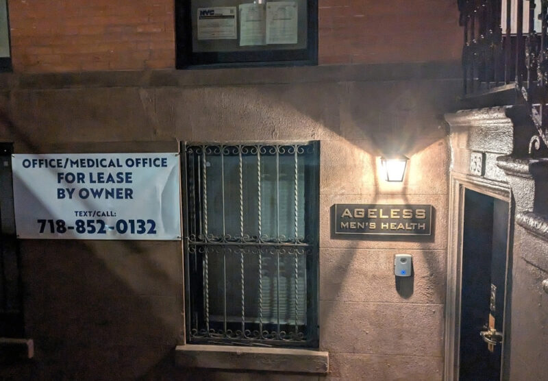 Photograph of empty brownstone store front at 153 Clinton Street in Brooklyn Heights. Between a window and a door on the ground level is a sign for Ageless Men's Health, the former tenant. To the right is a sign for the realtor with a phone number to call for prospective buyers.